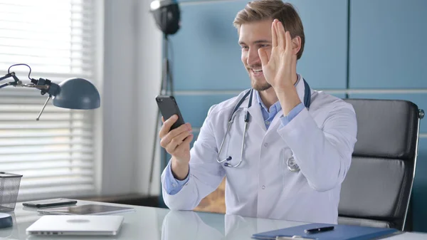 Доктор говорит на видео на смартфоне, сидя в клинике — стоковое фото