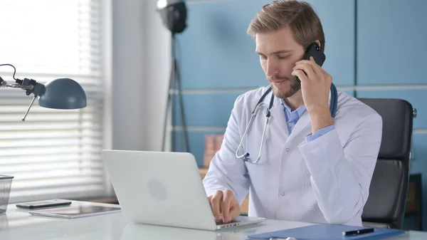 Doctor hablando por teléfono mientras trabaja en el ordenador portátil —  Fotos de Stock