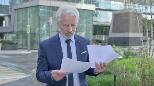 Old Businessman Reading Documents while Walking on the Street