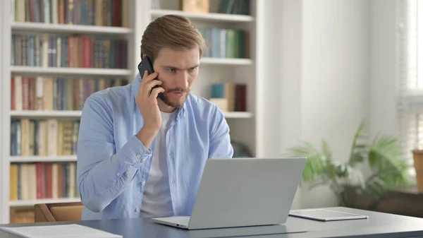 Uomo che parla al telefono durante l'utilizzo del computer portatile — Foto Stock