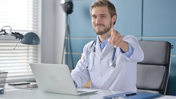 Lekarz wskazujący na kamerę podczas korzystania z laptopa w klinice — Zdjęcie stockowe