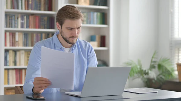 Mann liest Dokumente mit Laptop — Stockfoto