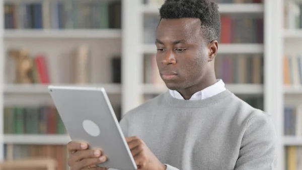 Portrét atraktivního afrického muže pomocí tabletu v knihovně — Stock fotografie