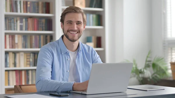 Uomo sorridente alla fotocamera durante l'utilizzo del computer portatile in ufficio — Foto Stock