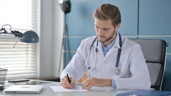 Doctor escribiendo en papel mientras está sentado en la clínica —  Fotos de Stock