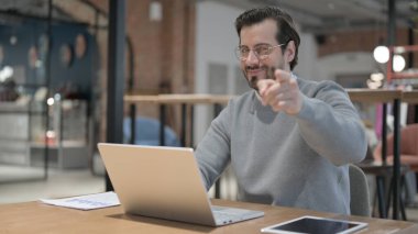 Ofiste dizüstü bilgisayar kullanırken kamerayı gösteren genç adam.