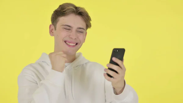 Young Man Celebrating on Smartphone on Yellow Background — Stock Photo, Image