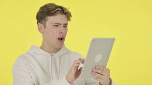 Молодий чоловік реагує на втрату планшета на жовтому тлі — стокове фото
