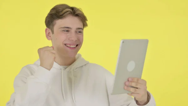 Mladý muž slaví úspěch na tabletu na žlutém pozadí — Stock fotografie
