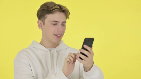 Молодий чоловік переглядає смартфон на жовтому тлі — стокове фото