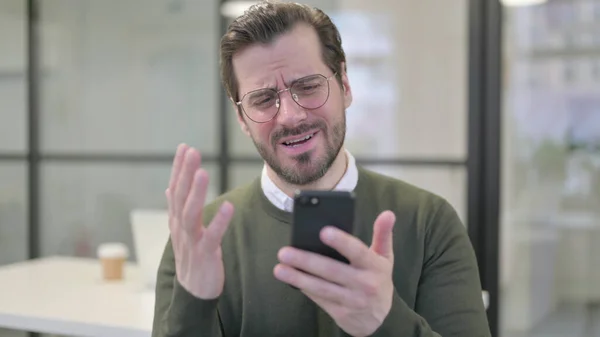 Retrato del joven empresario reaccionando a la pérdida en el teléfono inteligente —  Fotos de Stock