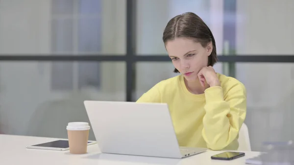 Młoda kobieta myśli podczas pracy na laptopie w biurze — Zdjęcie stockowe