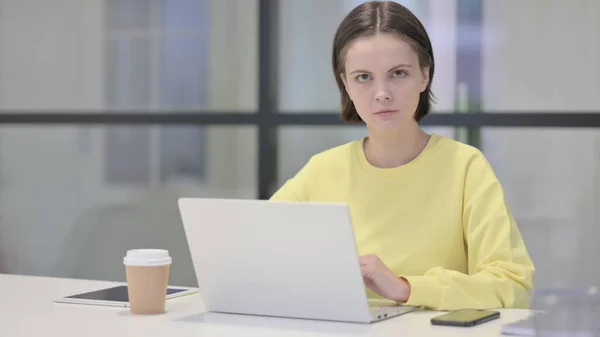 Mladá žena dívá na fotoaparát při používání notebooku v kanceláři — Stock fotografie