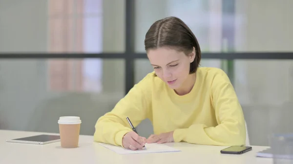 Jonge vrouw die op papier schrijft op kantoor — Stockfoto