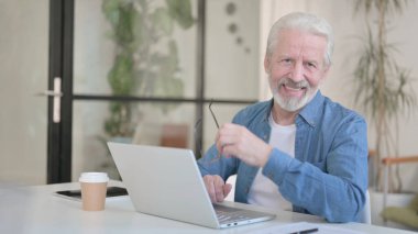 Senior Old Man Smiling at Camera while using Laptop