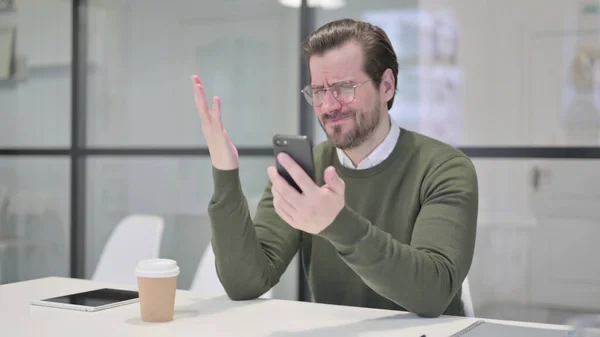 Расстроенный молодой бизнесмен реагирует на убытки на смартфоне — стоковое фото