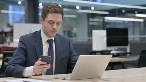 Empresario usando Smartphone mientras usa Laptop en Office — Vídeos de Stock