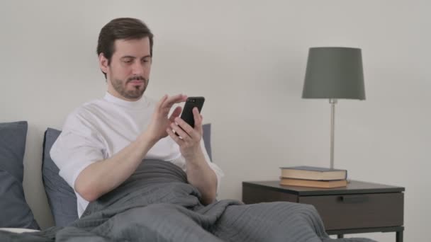 ベッドでスマホを使う若い男 — ストック動画