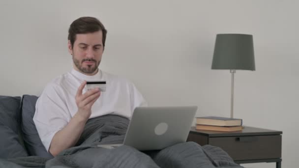 Homem jovem que faz o pagamento em linha no portátil na cama — Vídeo de Stock