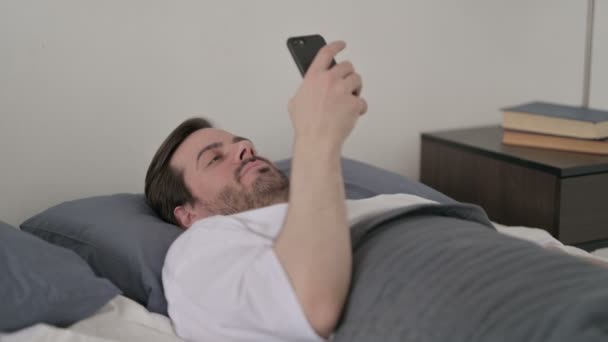 ベッドに横になりながらスマホを使う若者 — ストック動画