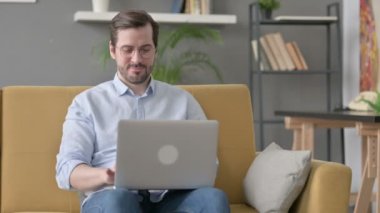 Genç adam kanepede dizüstü bilgisayarda çalışıyor. 
