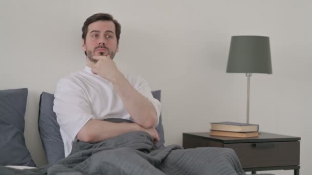 ベッドに座りながら考える若い男 — ストック動画