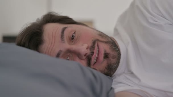 ベッドで寝ている間にビデオ通話で話している若い男の肖像 — ストック動画