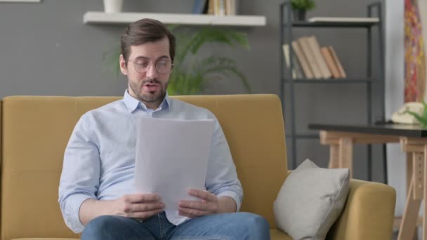 Jovem homem leitura papéis em voz alta no sofá — Vídeo de Stock