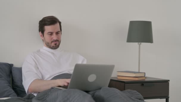 Молодий чоловік з болем у спині працює на ноутбуці в ліжку — стокове відео