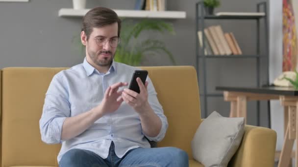 Молодий чоловік користується смартфоном на Софі — стокове відео