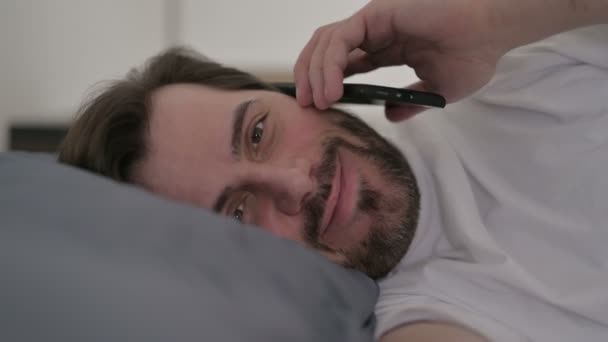 Portret van de jonge man praten op oproep op Smartphone in bed — Stockvideo