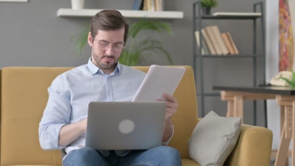 Jovem com Laptop Leitura Documentos no Sofá — Vídeo de Stock