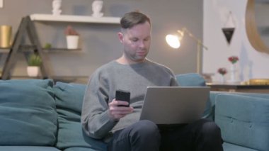 Dizüstü bilgisayarı olan sıradan bir adam koltukta Smartphone kullanıyor. 