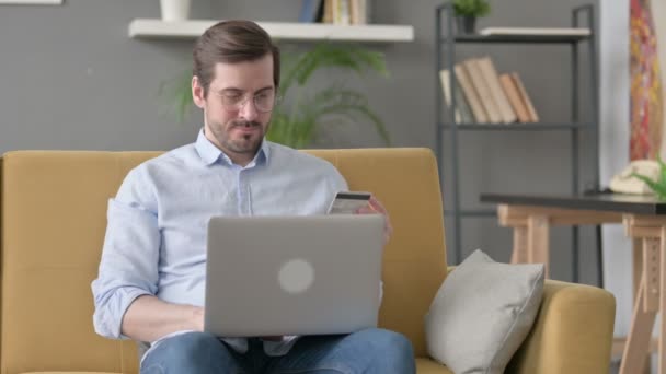 Junger Mann mit erfolgloser Online-Zahlung am Laptop auf Sofa — Stockvideo