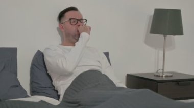 Middle Aged Man Coughing while Sitting in Bed