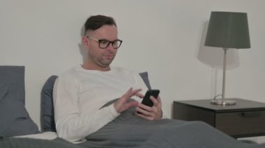 Orta yaşlı adam yatakta akıllı telefondan kaybına tepki veriyor.