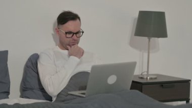 Middle Aged Man Thinking while Working on Laptop in Bed