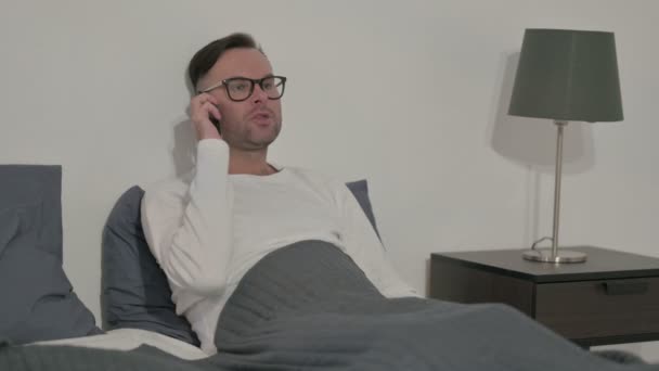 Angry Middle Aged Man Talking Smartphone While Sitting Bed — Stock video