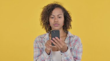 African Woman Browsing Smartphone on Yellow Background 