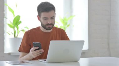 İş yerinde akıllı telefon kullanan yaratıcı genç adam.