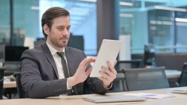 Young Businessman Browsing Internet on Tablet while Sitting in Office