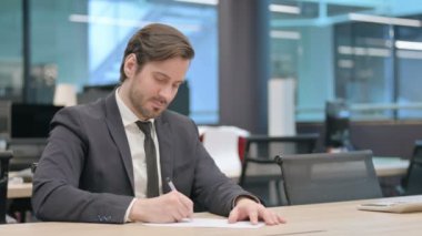Young Businessman Writing on Paper in Office, Paperwork