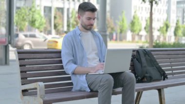 Adam bankta otururken dizüstü bilgisayar kullanıyor