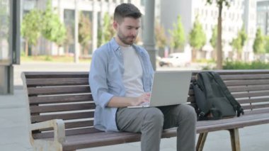 Man Reacting to Loss on Laptop while Sitting on Bench