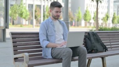 Man Pointing at the Camera while Sitting on Bench Outdoor