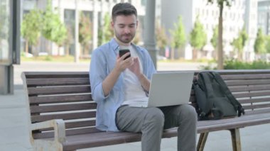 Man Talking on Phone and using Laptop while Sitting on Bench