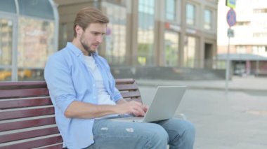 Orta yaşlı adam dışarıda Bench 'te otururken dizüstü bilgisayarda kaybına tepki veriyor.