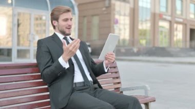 Online Video Chat on Tablet by Middle Aged Businessman Sitting Outdoor on Bench 