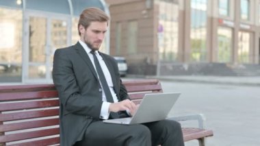 Middle Aged Businessman Reacting to Loss on Laptop while Sitting Outdoor on Bench