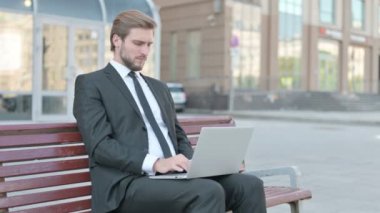 Middle Aged Businessman with Neck Pain Using Laptop while Sitting Outdoor on Bench